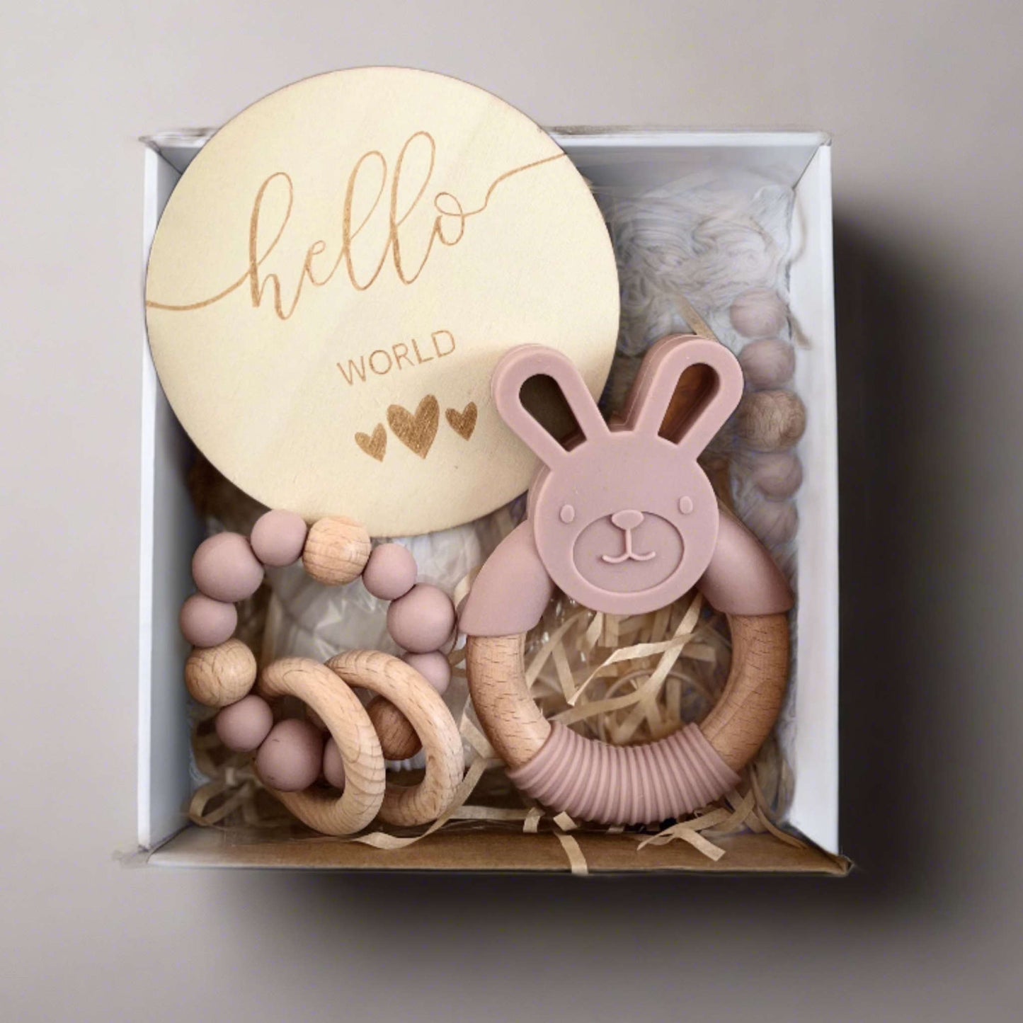 Discover the perfect baby shower gift with our Welcome to the World Baby Gift Box. Includes a 'Hello World' wooden disc, rose pink silicone teether, white muslin hairband, and a pacifier with wooden and silicone beads. Beautifully packaged in pink, ideal for celebrating a new arrival.